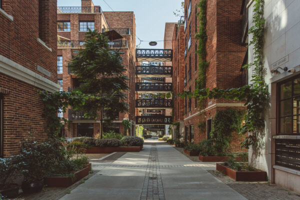 Moderne straat tussen bakstenen gebouwen aan de Karl Weisbardstraat, met groene gevelbeplanting en loopbruggen tussen de gebouwen.